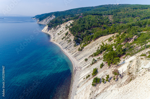 The coast of the Black sea near Gelendzhik. High layered rocks covered with pine trees. Gorges form a descent to the sea. A small pebble beach at the foot of the cliffs