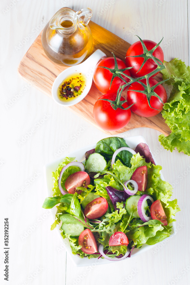 Fresh healthy vegetable salad made of cherry tomato, ruccola, feta, olives, cucumbers, onion and spices. Greek, Caesar salad in a white bowl on wooden background. Healthy organic diet food concept. Fresh healthy vegetable salad made of cherry tomato, ruccola, feta, olives, cucumbers, onion and spices. Greek, Caesar salad in a white bowl on wooden background. Healthy organic diet food concept.