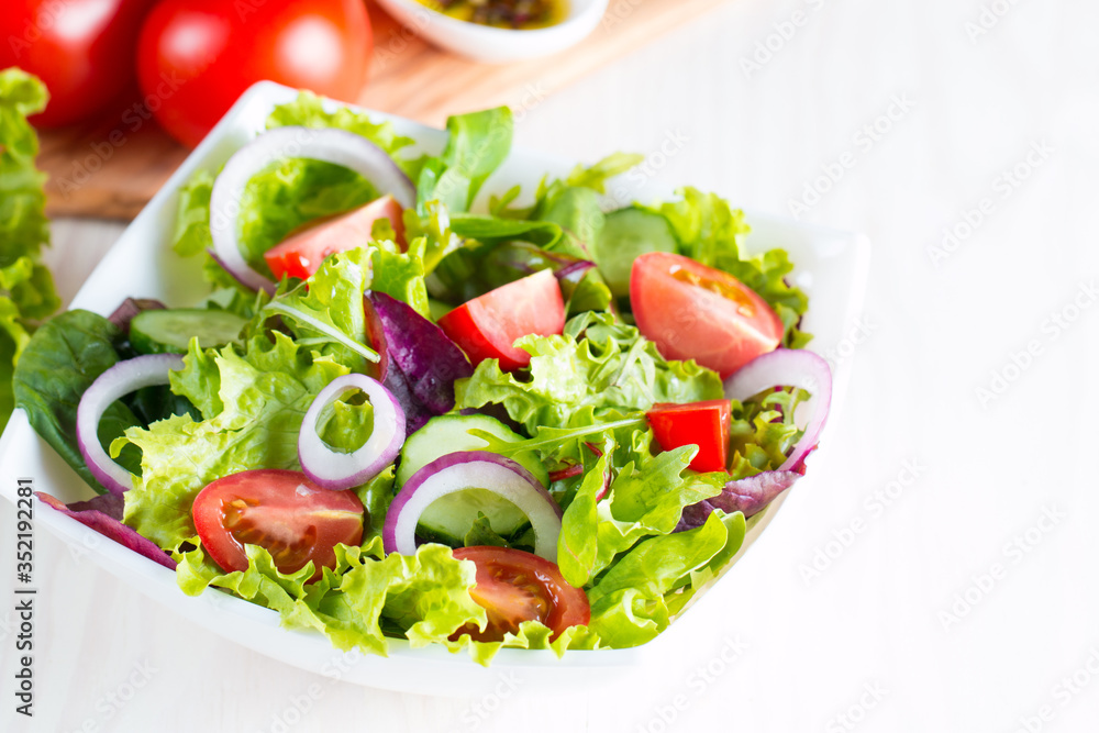 Fresh healthy vegetable salad made of cherry tomato, ruccola, feta, olives, cucumbers, onion and spices. Greek, Caesar salad in a white bowl on wooden background. Healthy organic diet food concept. Fresh healthy vegetable salad made of cherry tomato, ruccola, feta, olives, cucumbers, onion and spices. Greek, Caesar salad in a white bowl on wooden background. Healthy organic diet food concept.