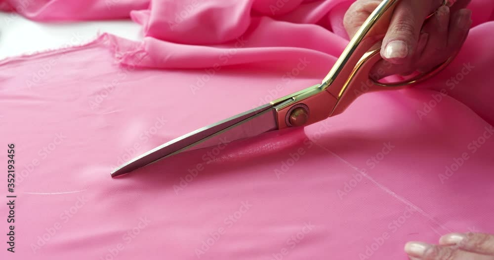 Beautiful close view of female hand cutting pink fabric with scissors Beautiful close view of female hand cutting pink fabric with scissors