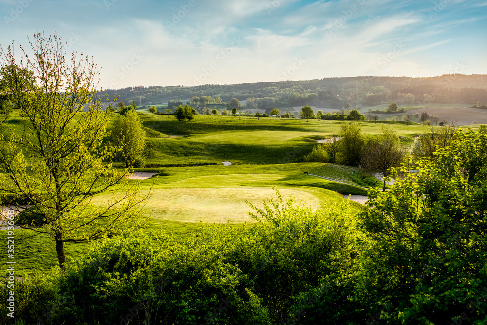 Obraz premium spring looking grassland, small gold course and flowers with sunrays in the sunrise