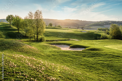 spring looking grassland, small gold course and flowers with sunrays in the sunrise