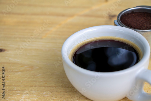 Black coffee in a white cup on natural color wooden table, focus on inner edge of the cup. Relaxing time concept.