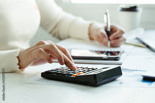 Tax concept.Woman hand using calculator and writing make note with calculate about cost at home office.Work from home