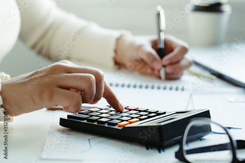 Tax concept.Woman hand using calculator and writing make note with calculate about cost at home office.Work from home