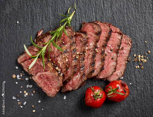 Grilled sliced beef steak with tomatoes on black background top view