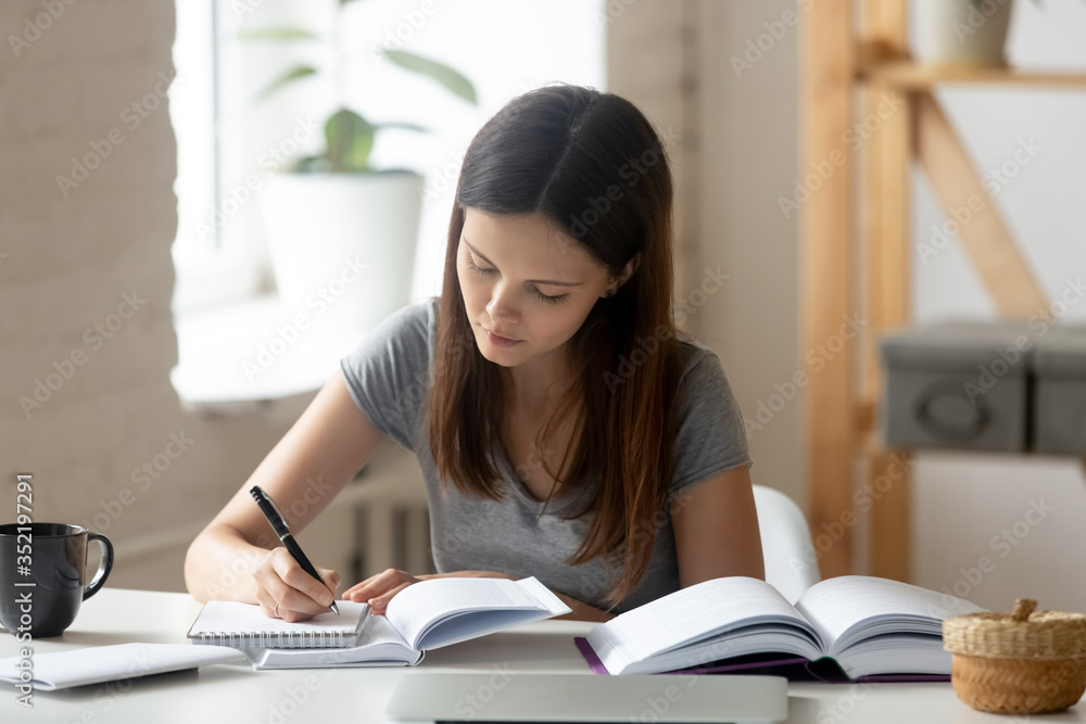 Smart female Caucasian student handwriting make notes preparing for exam or test at home, concentrated millennial girl study using textbooks, do homework or research, education concept Smart female Caucasian student handwriting make notes preparing for exam or test at home, concentrated millennial girl study using textbooks, do homework or research, education concept