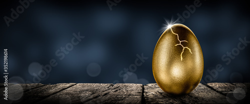 Obraz na plátně Shiny Golden Nest Egg On Wooden Table Cracking Open With Burst Of Light - Invest