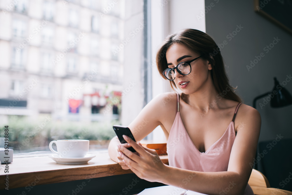 Focused young woman messaging on smartphone during coffee break in cozy cafeteria Focused young woman messaging on smartphone during coffee break in cozy cafeteria