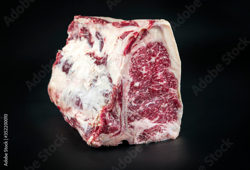 Raw dry aged wagyu porterhouse beef block offered as closeup on black background with copy space