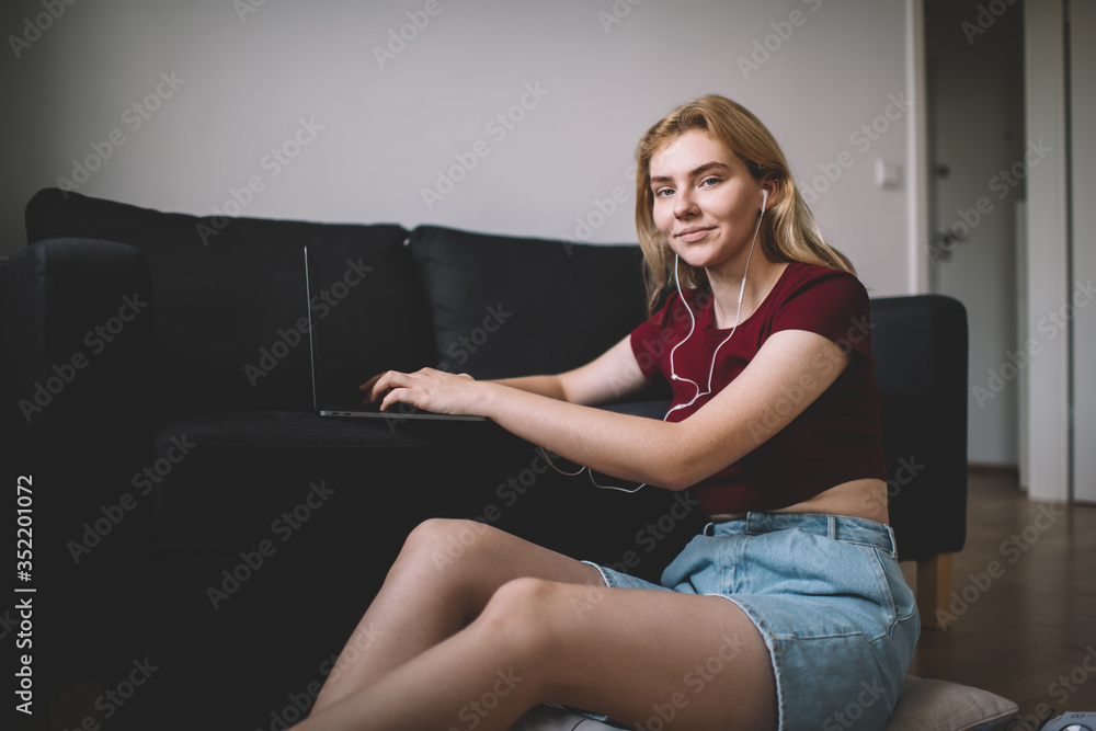 Positive young woman typing on laptop in living room