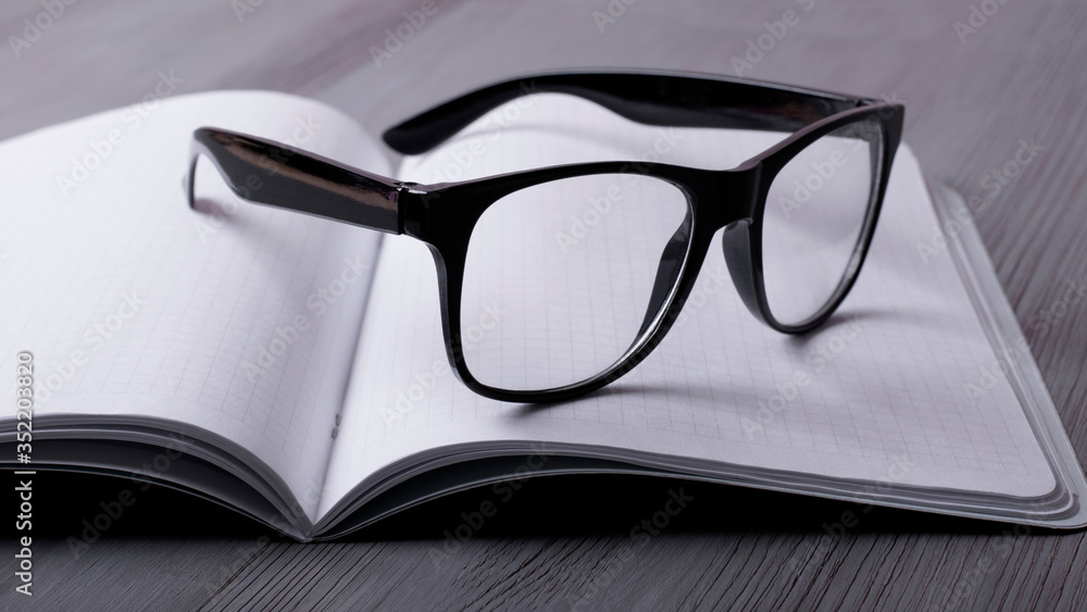 Glasses on the open blank notebook on the grey desktop Glasses on the open blank notebook on the grey desktop