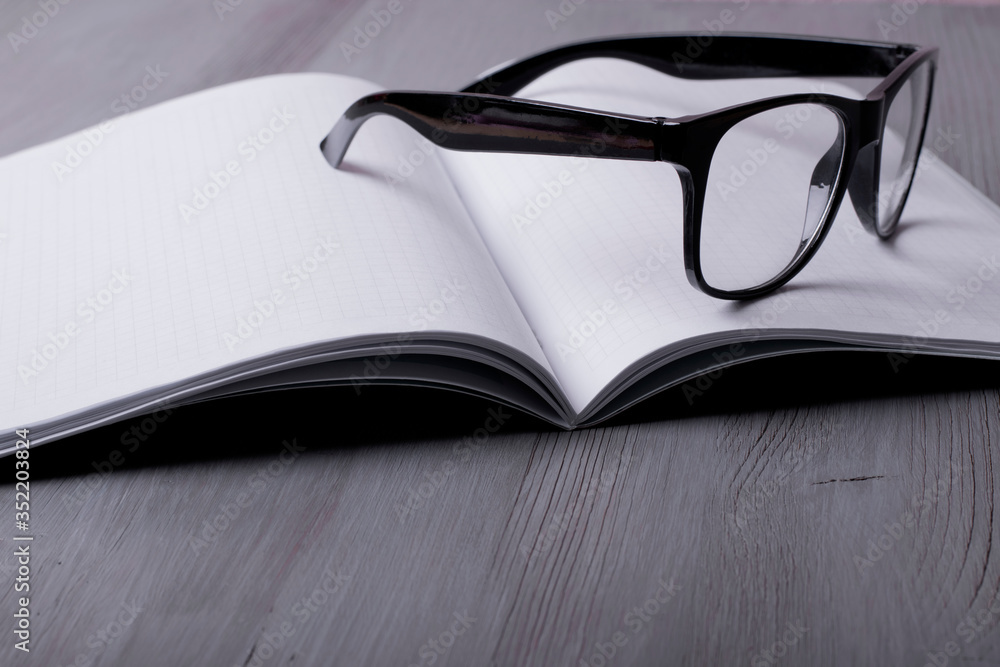 Glasses on the open blank notebook on the grey desktop Glasses on the open blank notebook on the grey desktop