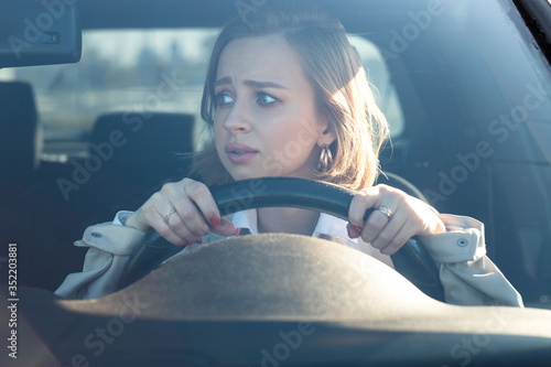 Woman drives her car for the first time, tries to avoid a car accident, is very nervous and scared, worries, clings tightly to the wheel. Inexperienced driver in stress and confusion after an accident photo