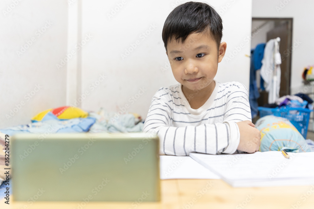 Home school and new normal lifestyle concepts.Asian boy studying through online media and do homework at home due to social distance policy to prevent the spread of the coronavirus(Covid-19) Home school and new normal lifestyle concepts.Asian boy studying through online media and do homework at home due to social distance policy to prevent the spread of the coronavirus(Covid-19)