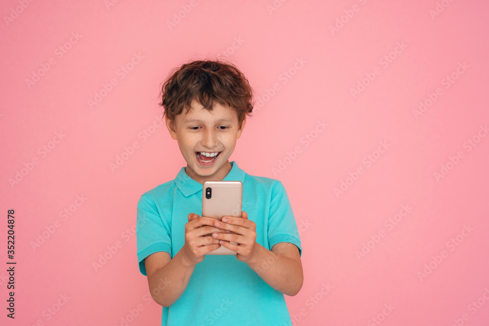 cheerful boy dressed in a Polo shirt, holding a smartphone on a pink background. cheerful boy dressed in a Polo shirt, holding a smartphone on a pink background.