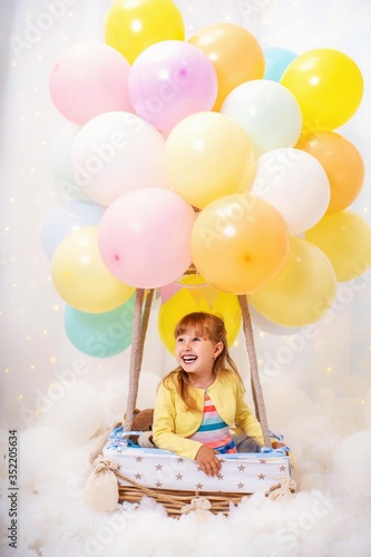 laughing little girl sits in basket decorative balloon and looking away.