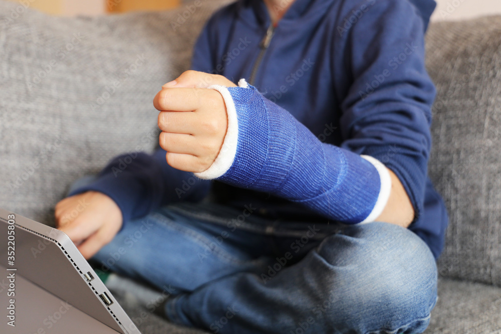 Junge mit Gipsarm sitzt mit dem Tablet auf dem Sofa (Model released) Junge mit Gipsarm sitzt mit dem Tablet auf dem Sofa (Model released)