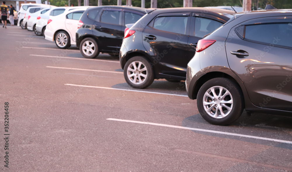 Closeup of rear, back side of black car with  other cars parking in outdoor parking area in twilight evening. 