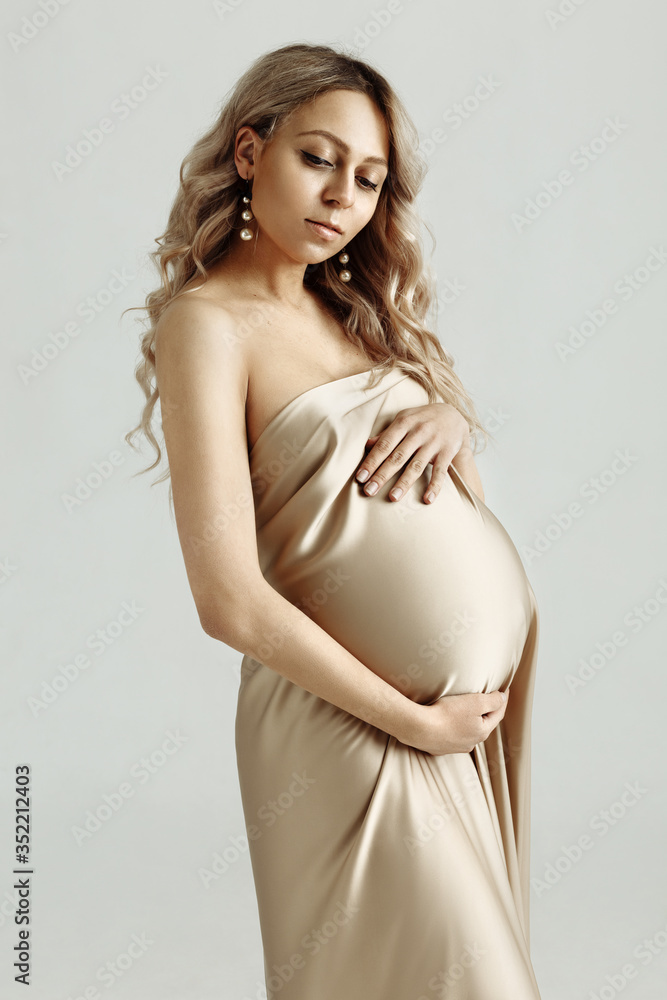 Pretty pregnant woman in a beige satin dress touching her big belly. Close up. Motherhood, pregnancy, people and expectation concept. Pregnant girl expecting baby. Isolated Pretty pregnant woman in a beige satin dress touching her big belly. Close up. Motherhood, pregnancy, people and expectation concept. Pregnant girl expecting baby. Isolated