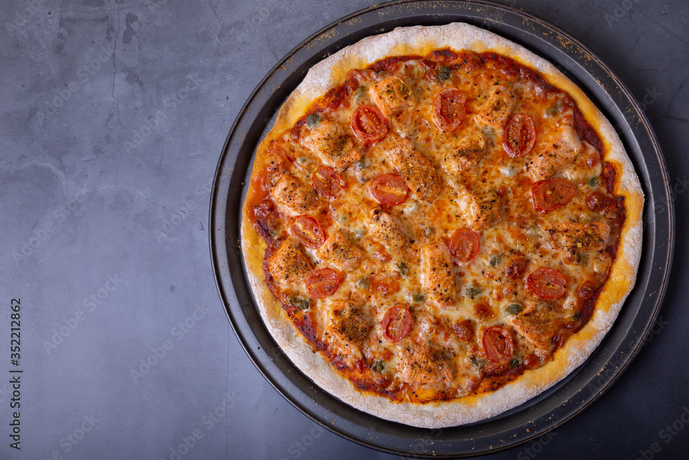 Pizza with salmon, tomatoes and capers. Whole pizza on a black background. Close-up, top view, place for text. Pizza with salmon, tomatoes and capers. Whole pizza on a black background. Close-up, top view, place for text.