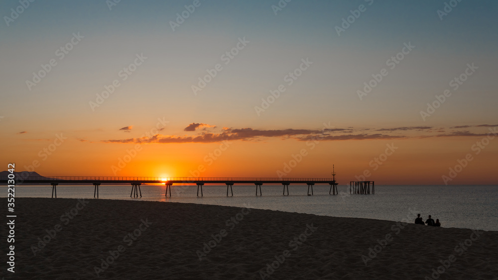 Obraz premium group of friends sitting on the beach watching the sunrise