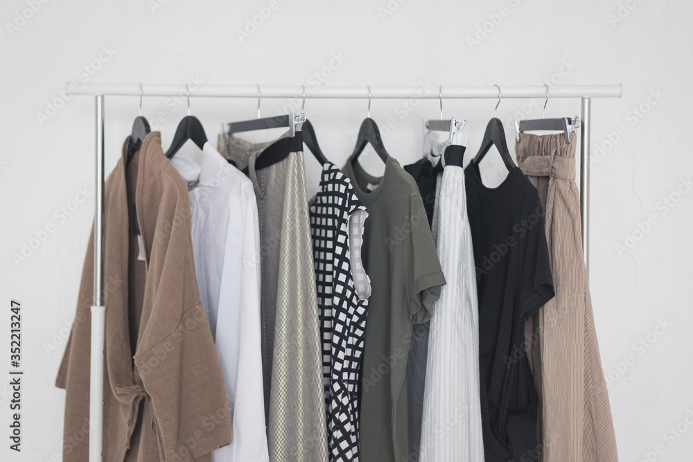 A rack with stylish clothes next to a white wall in the room. Clothing retails concept. Advertise, sale, fashion. A rack with stylish clothes next to a white wall in the room. Clothing retails concept. Advertise, sale, fashion.