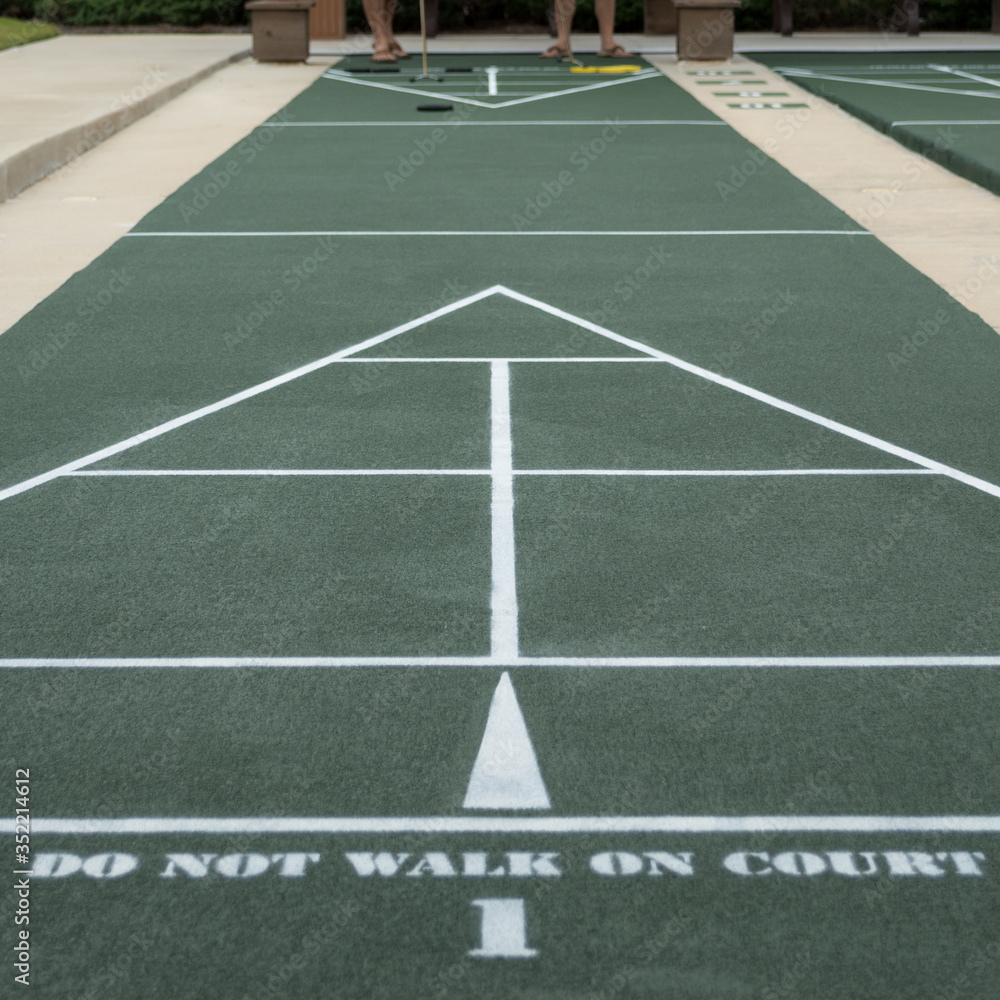 The legs of two players at the end of a shuffleboard court, a popular hobby among retired seniors