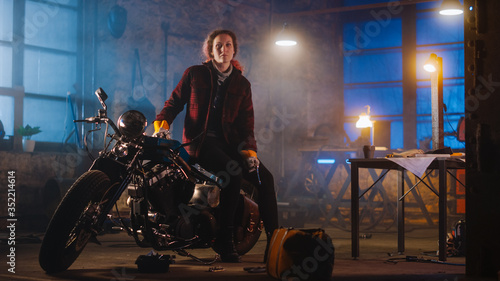 Young Authentic Female Mechanic is Sitting on a Custom Bobber Motorbike and Posing in Workwear with Ratchet and Spanner. Talented Girl Wearing a Checkered Shirt. Creative Workshop Garage.