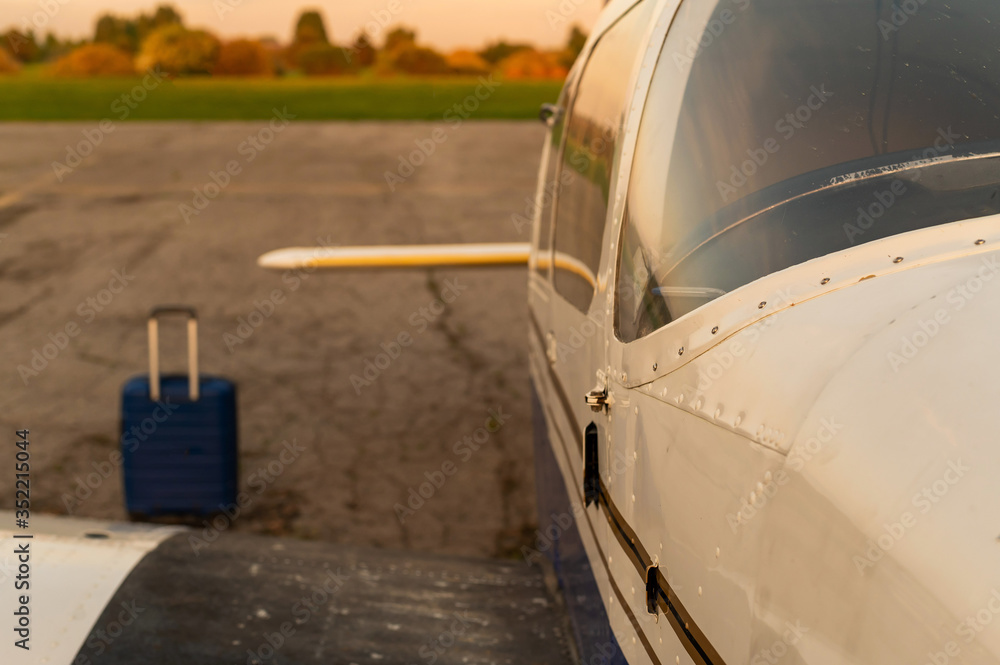 A blue suitcase and a parked small private jet. Quadruple plane with a propeller for an air taxi in the sunset. Self travel concept. plane for VIP persons. A blue suitcase and a parked small private jet. Quadruple plane with a propeller for an air taxi in the sunset. Self travel concept. plane for VIP persons.