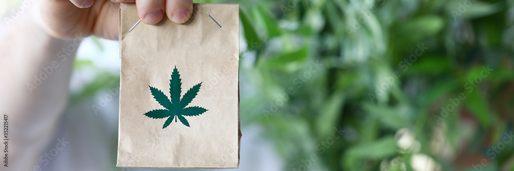 Male hand hold paper packet with marijuana symbol closeup background