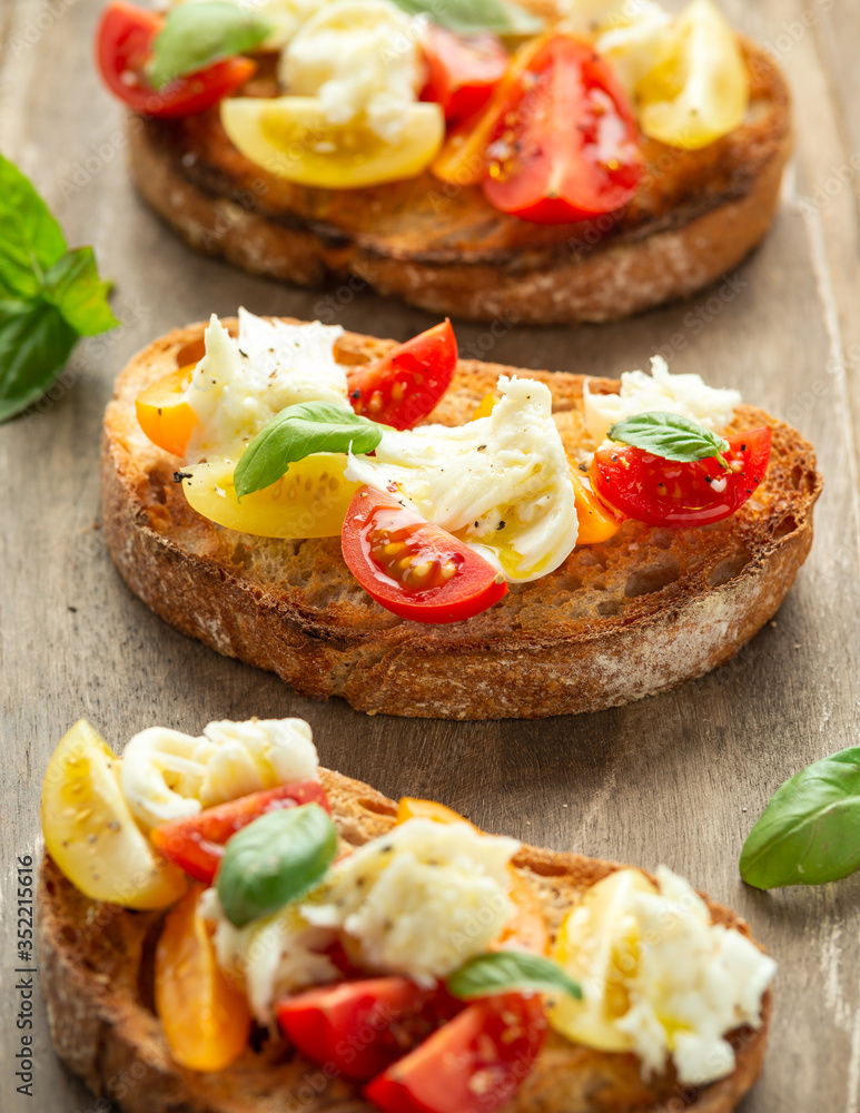 Tomato bruschetta and mozzarella cheese with basil on a rustic wooden board Tomato bruschetta and mozzarella cheese with basil on a rustic wooden board