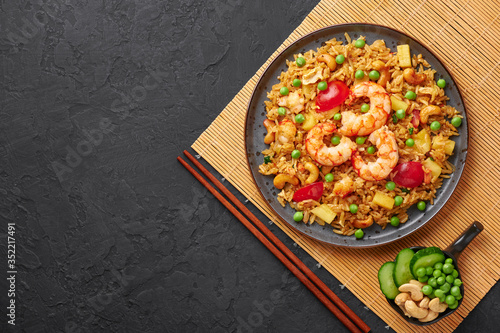 Thai Pineapple Fried Rice or Kao Pad Sapparod on a black plate on dark slate backdrop. Kao Pad Sapparod is a Thai Cuisine dish with rice, shrimps, pineapple, tomatoes and cashew nuts. Copy space