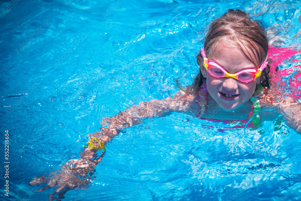 Naklejka premium Portrait of little cute young girl in water glasses practice swimming in the outdoor pool. The child in the outdoor pool at the resort.