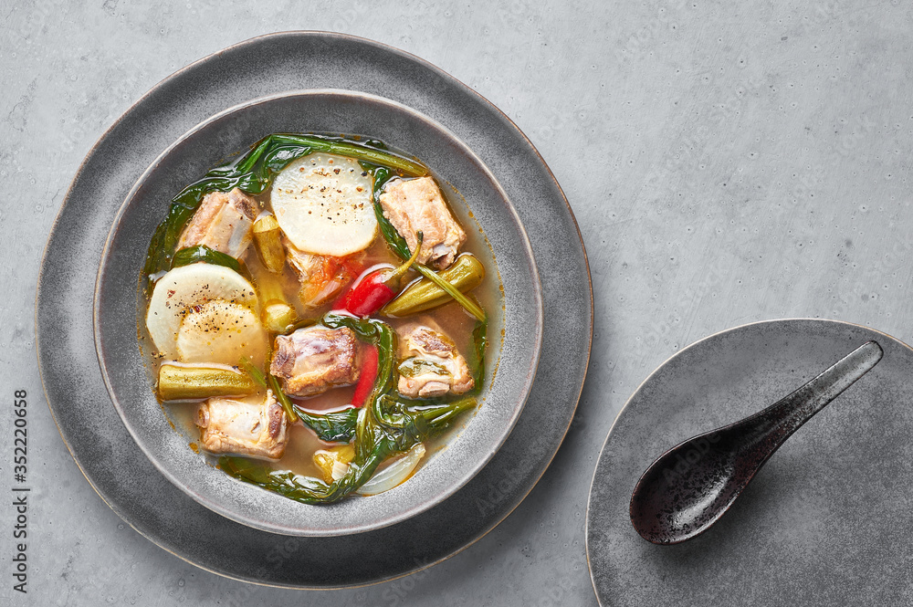 Sinigang na Baboy or Filipino Pork Meat Soup in gray bowl on concrete backdrop. Sinigang is a Filipino cuisine dish with meat, bamia, daikon, spinach, fish sauce. Filipino Food. Asian Meal. Copy space Sinigang na Baboy or Filipino Pork Meat Soup in gray bowl on concrete backdrop. Sinigang is a Filipino cuisine dish with meat, bamia, daikon, spinach, fish sauce. Filipino Food. Asian Meal. Copy space