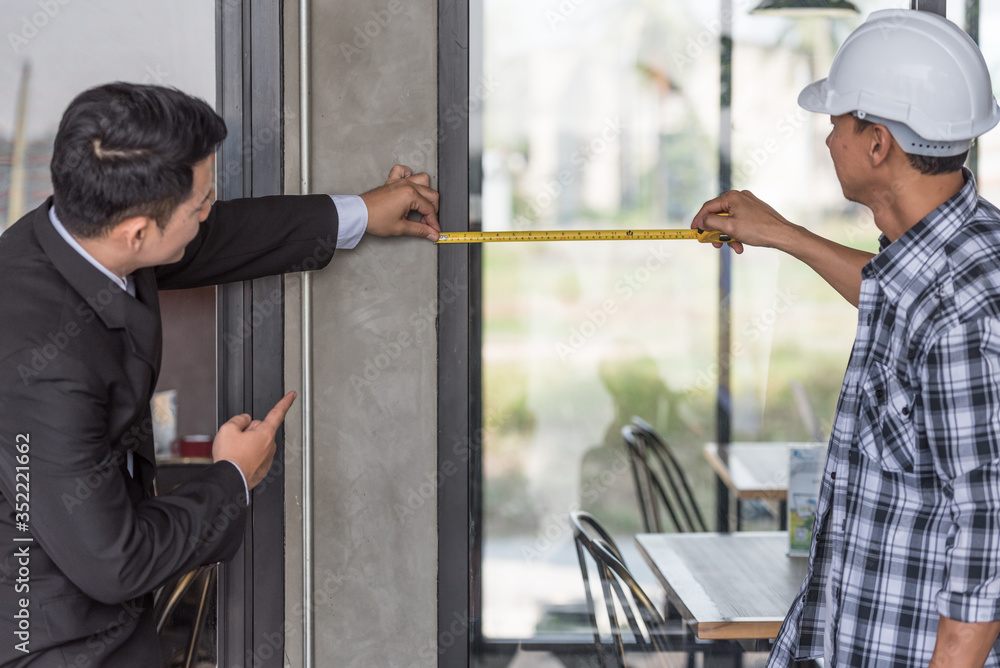 Businessman hiring renovation contractors using measure tape to mark on glass window frame for decorate office for new project. Businessman hiring renovation contractors using measure tape to mark on glass window frame for decorate office for new project.