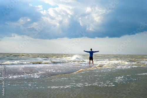 a man stands with outstretched arms on the edge of the earth in the middle of the sea waves in Sunny weather
