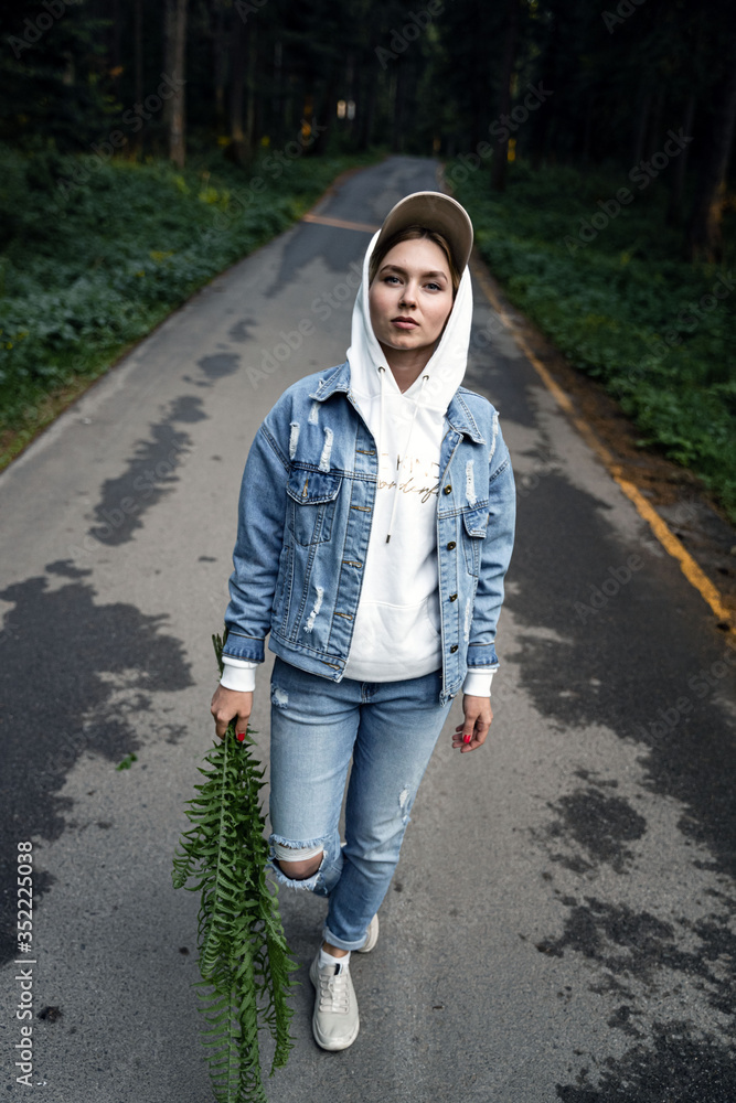 Fototapeta premium girl in a denim suit walks through the woods in the hands of a fern