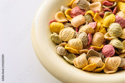 uncooked colored homemade pasta in a bowl close-up on a white table, top view