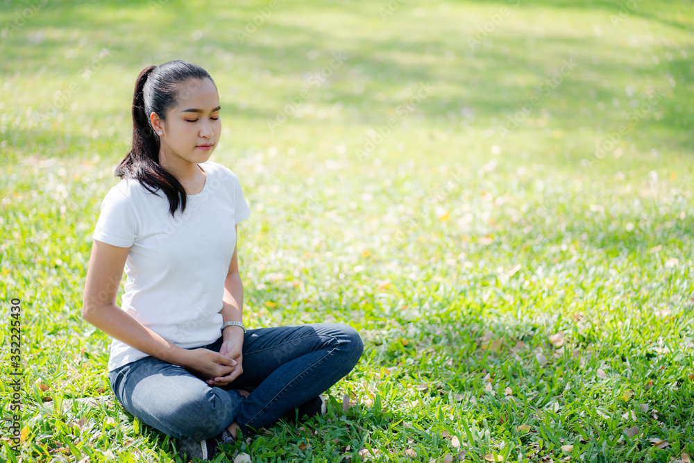 Asian young women meditation yoga with smile face for peace, relaxation emotional on green grass of park with natural light sunset of the sun with dramatic yellow and orange sky. Image depth of field. Asian young women meditation yoga with smile face for peace, relaxation emotional on green grass of park with natural light sunset of the sun with dramatic yellow and orange sky. Image depth of field.