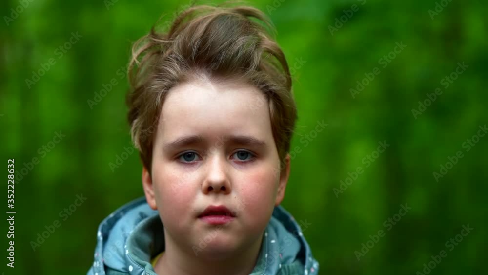 Sad girl thinks and looks at the camera. The face of a small, serious, sad child. Close-up portrait on a green background of foliage