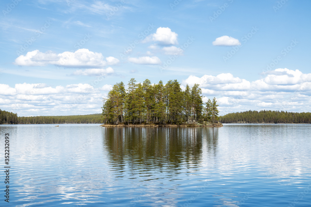 View of an idyllic lake with a small island in a Swedish forest. Blue sky and reflections on water. National Park. Summer in Scandinavia.