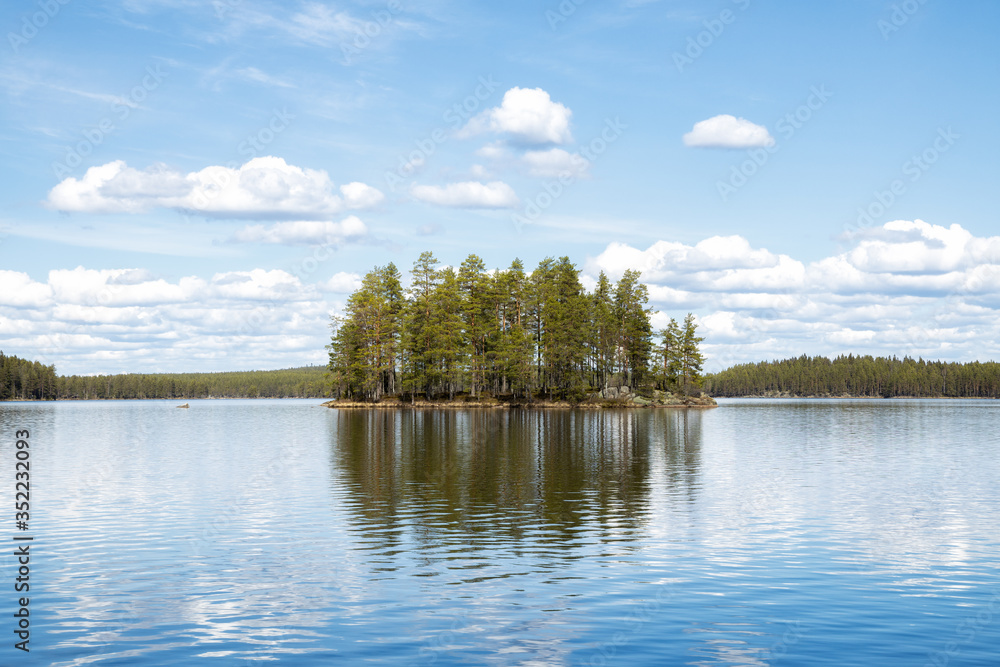 View of an idyllic lake with a small island in a Swedish forest. Blue sky and reflections on water. National Park. Summer in Scandinavia. View of an idyllic lake with a small island in a Swedish forest. Blue sky and reflections on water. National Park. Summer in Scandinavia.