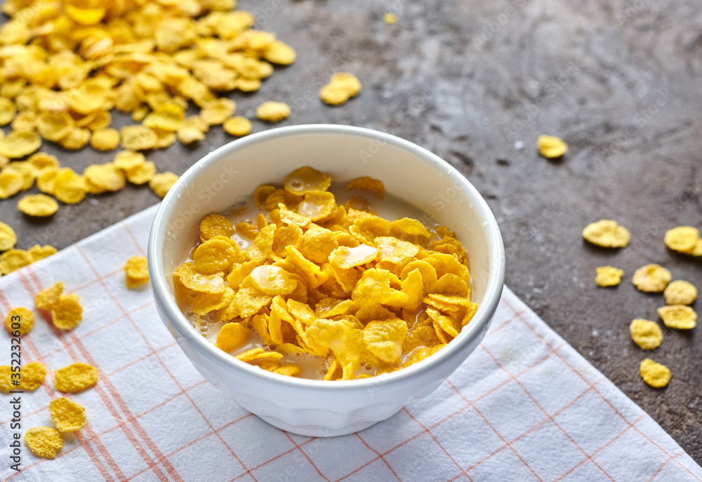yellow cornflakes with milk in a white deep plate on a brown table yellow cornflakes with milk in a white deep plate on a brown table