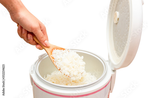 Women hand holding and using wood ladle to scoop steamed rice from electric rice cooker isolated on white background
