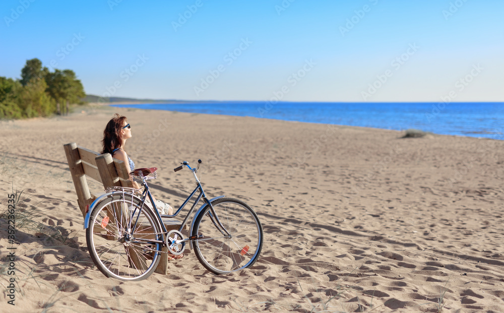 Fototapeta premium Middle-aged woman came on a Bicycle to the beach and resting sitting on a bench.