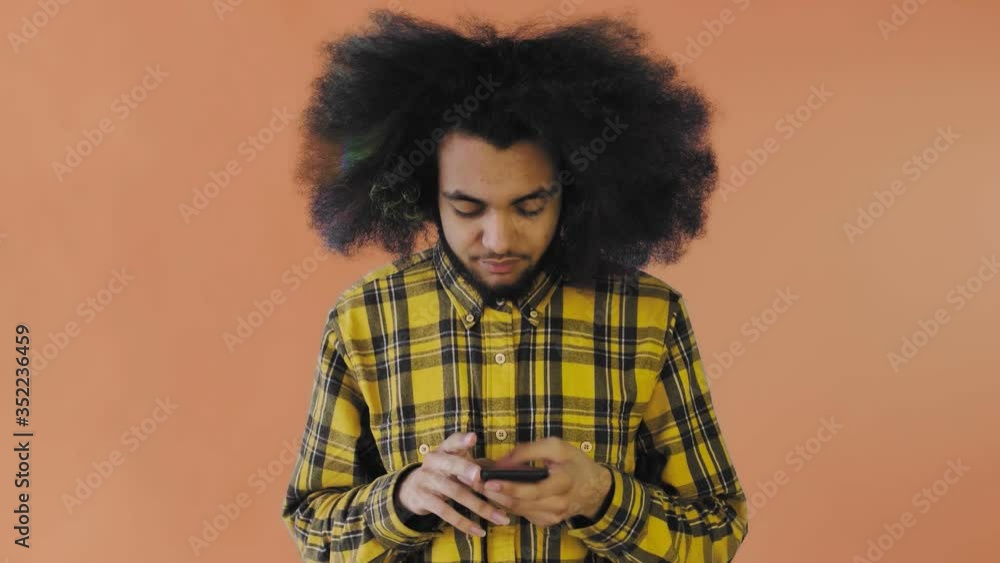 Frustrated young African American man holding broken mobile phone on Orange background. Concept of emotions Frustrated young African American man holding broken mobile phone on Orange background. Concept of emotions