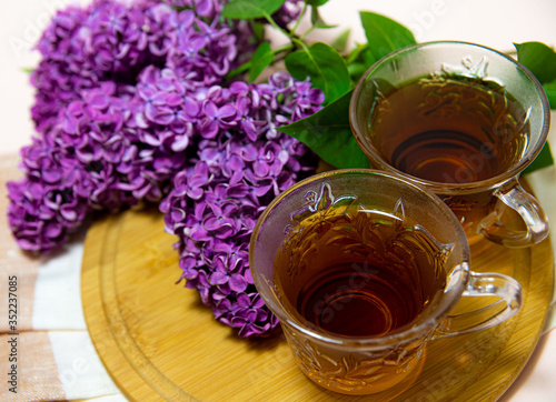  two cups with black tea and a branch of lilac with green leaves