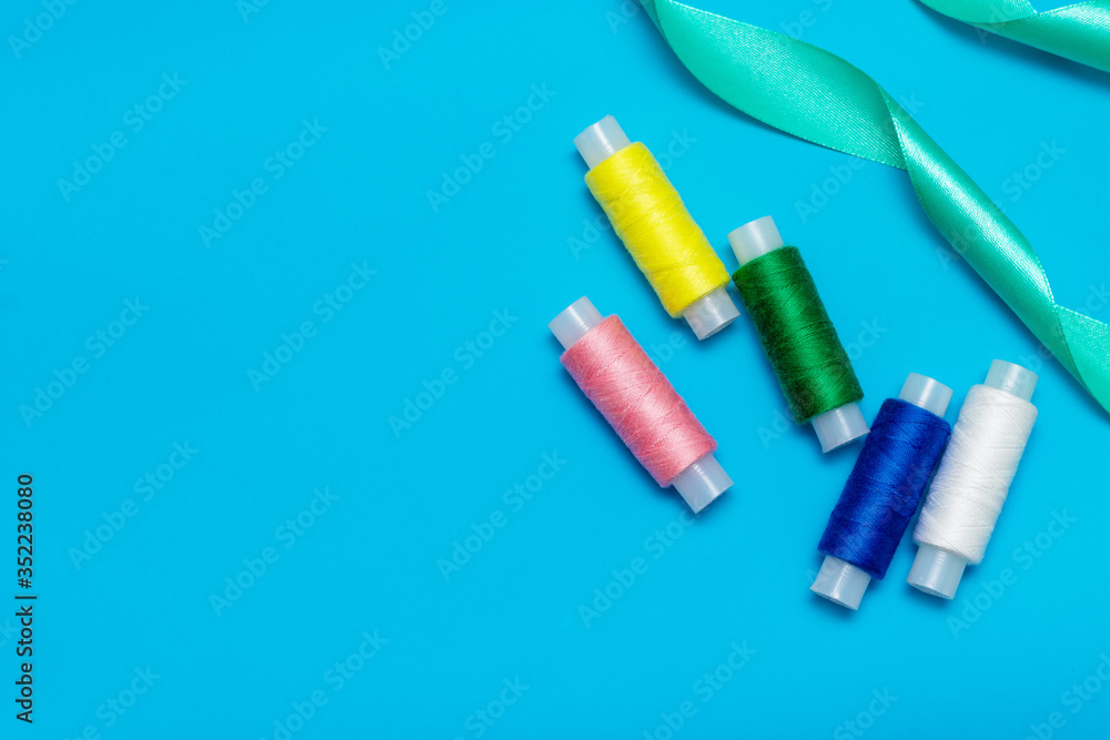 white, blue, green, pink, yellow thread and turquoise ribbon on a blue background, copy space, top view white, blue, green, pink, yellow thread and turquoise ribbon on a blue background, copy space, top view