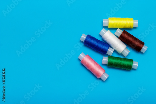 white, blue, green, pink, yellow thread and turquoise ribbon on a blue background, copy space, top view